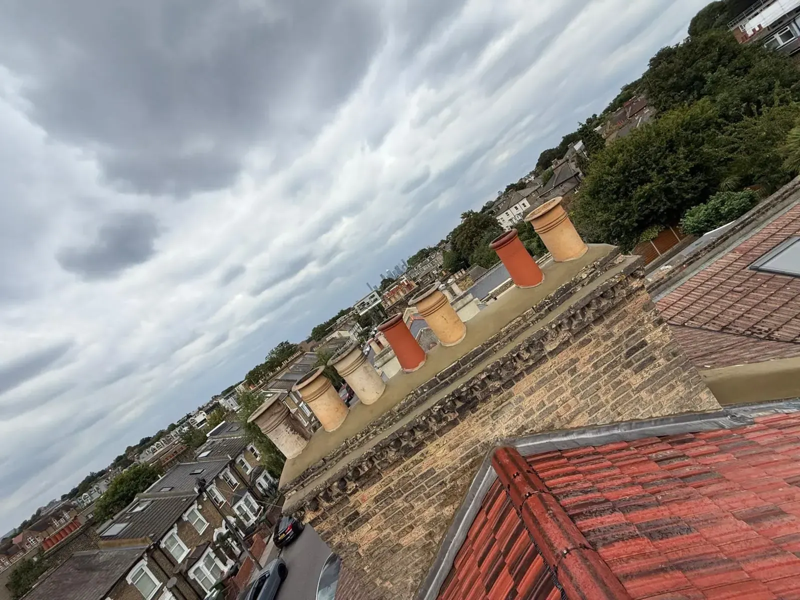 Repointed brick chimney with a row of terracotta pots and fresh flaunching above rooftops with the London skyline behind