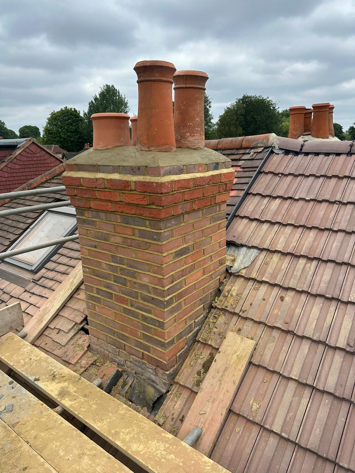 Rebuilt brick chimney stack on a tiled roof with scaffolding in place