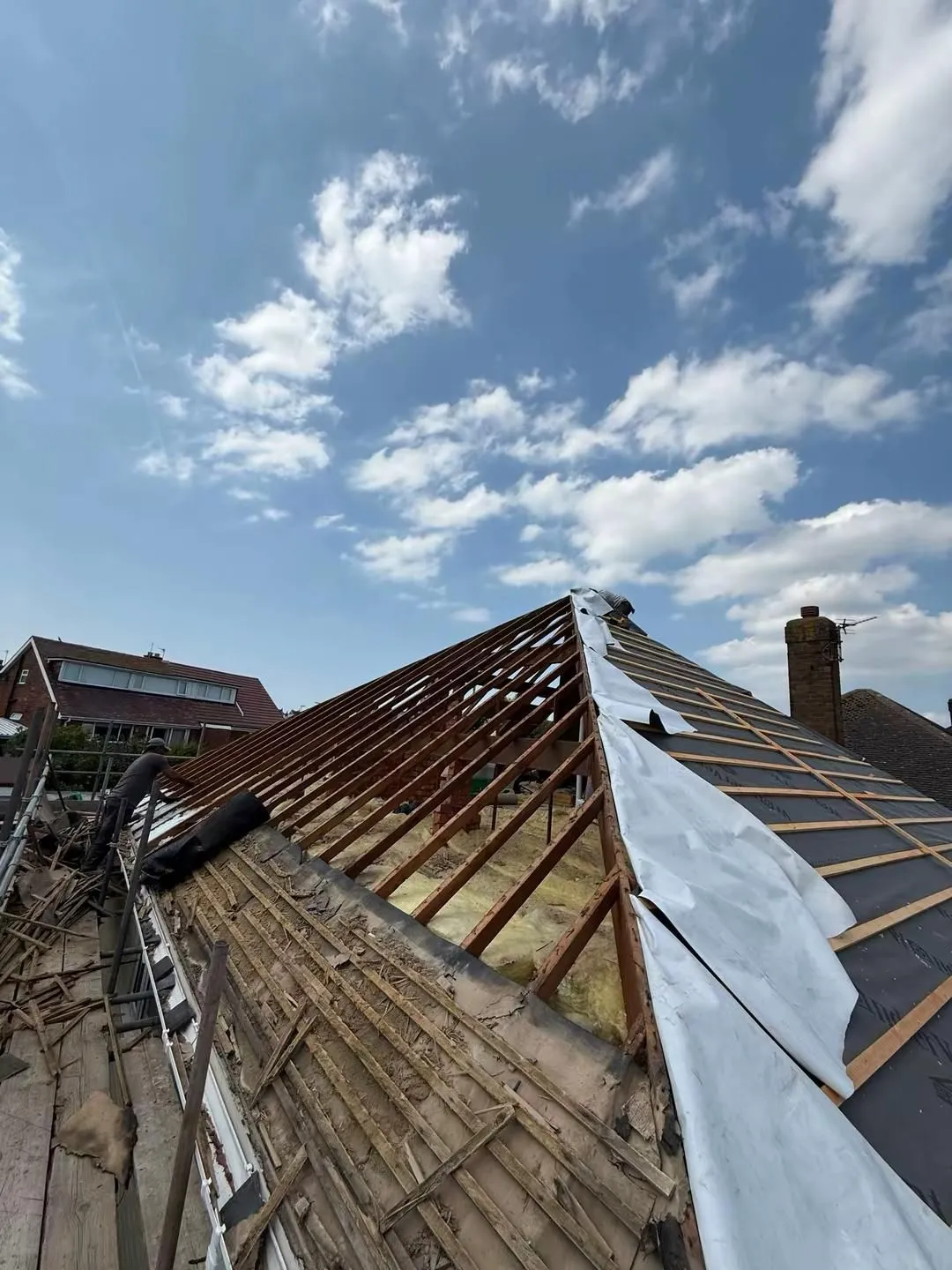 Hipped roof mid strip and re-roof: exposed rafters on one side, new breathable underlay and treated battens on the other