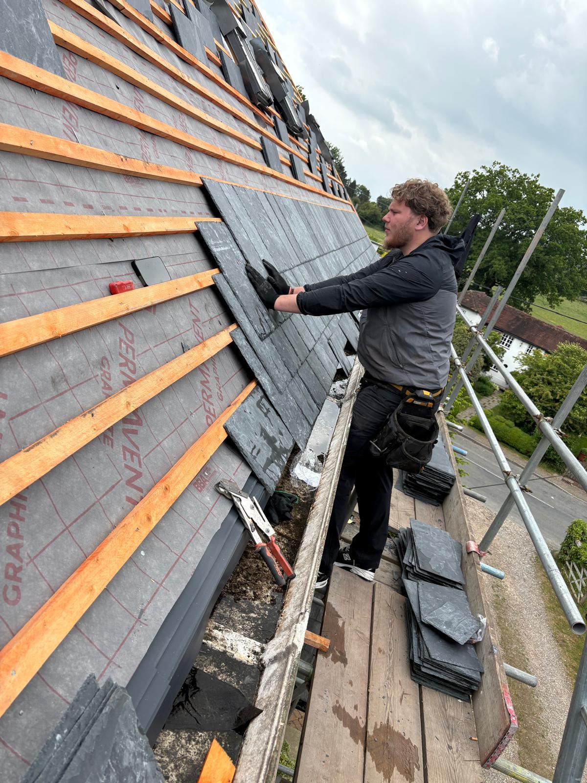 Roofer fixing natural slates to new battens over breathable membrane