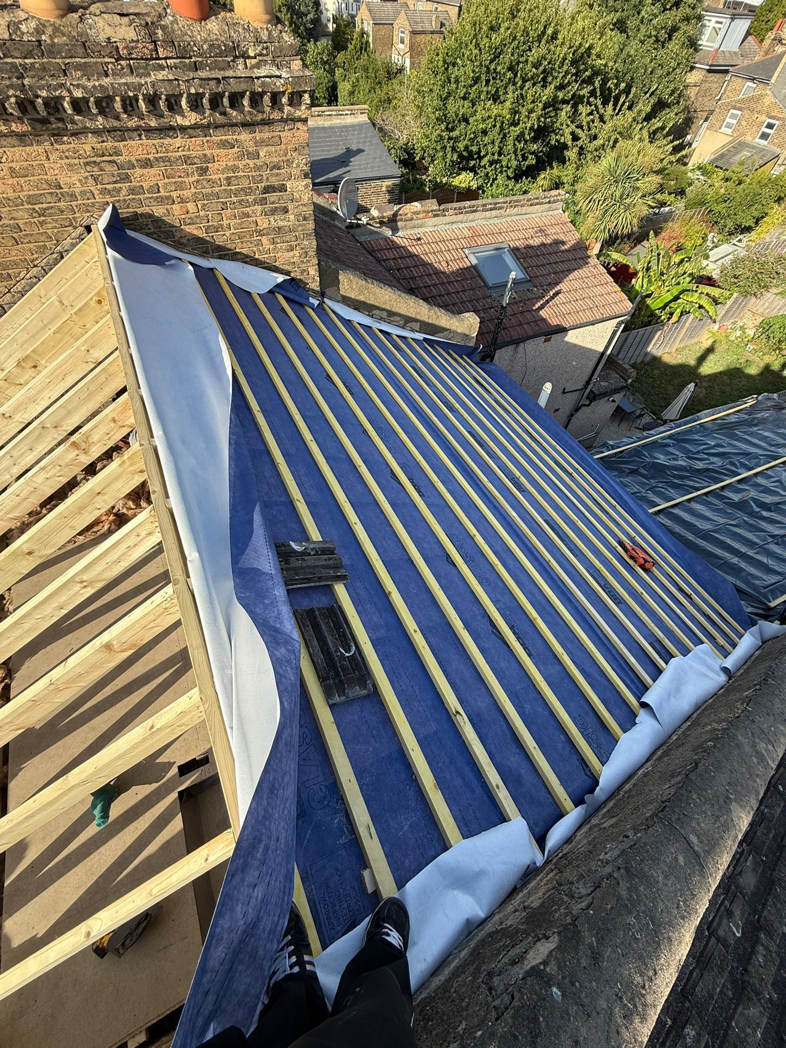 Timber rafters with breathable underlay and new battens beside a brick chimney stack