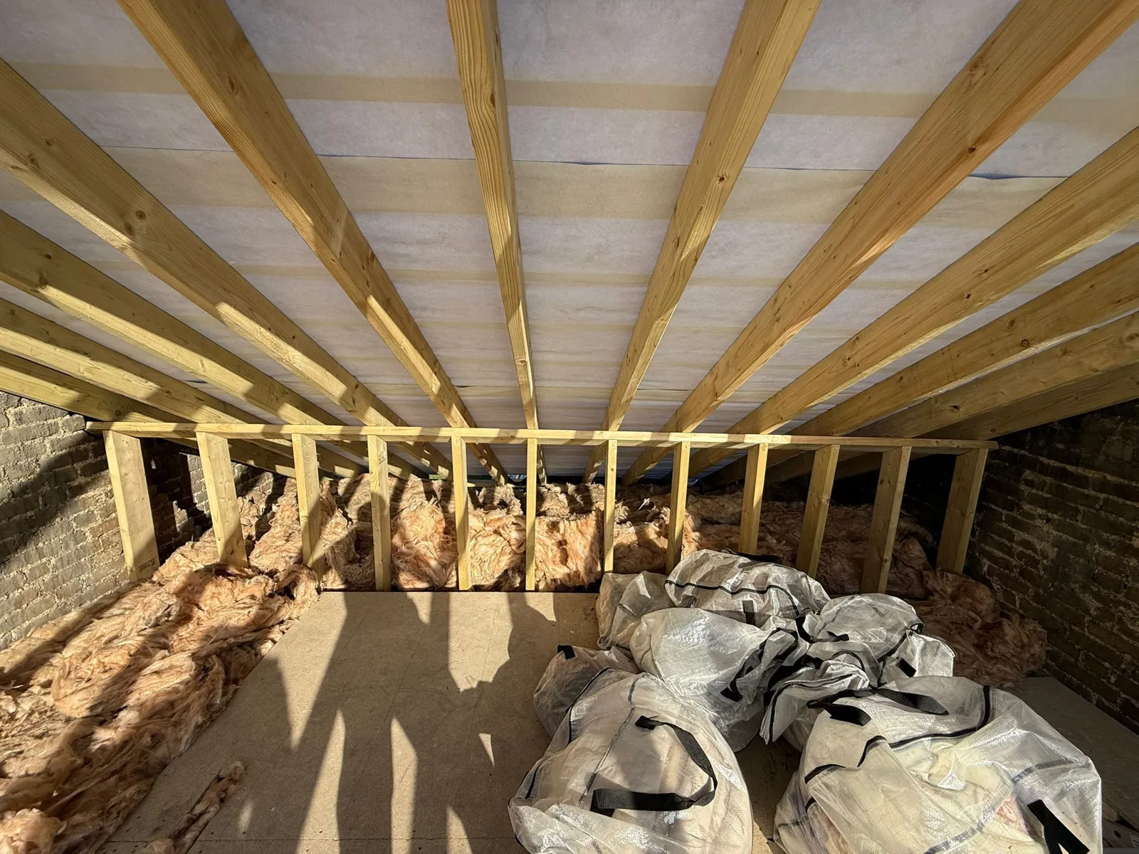 Timber roof framing seen from the loft with insulation between the joists