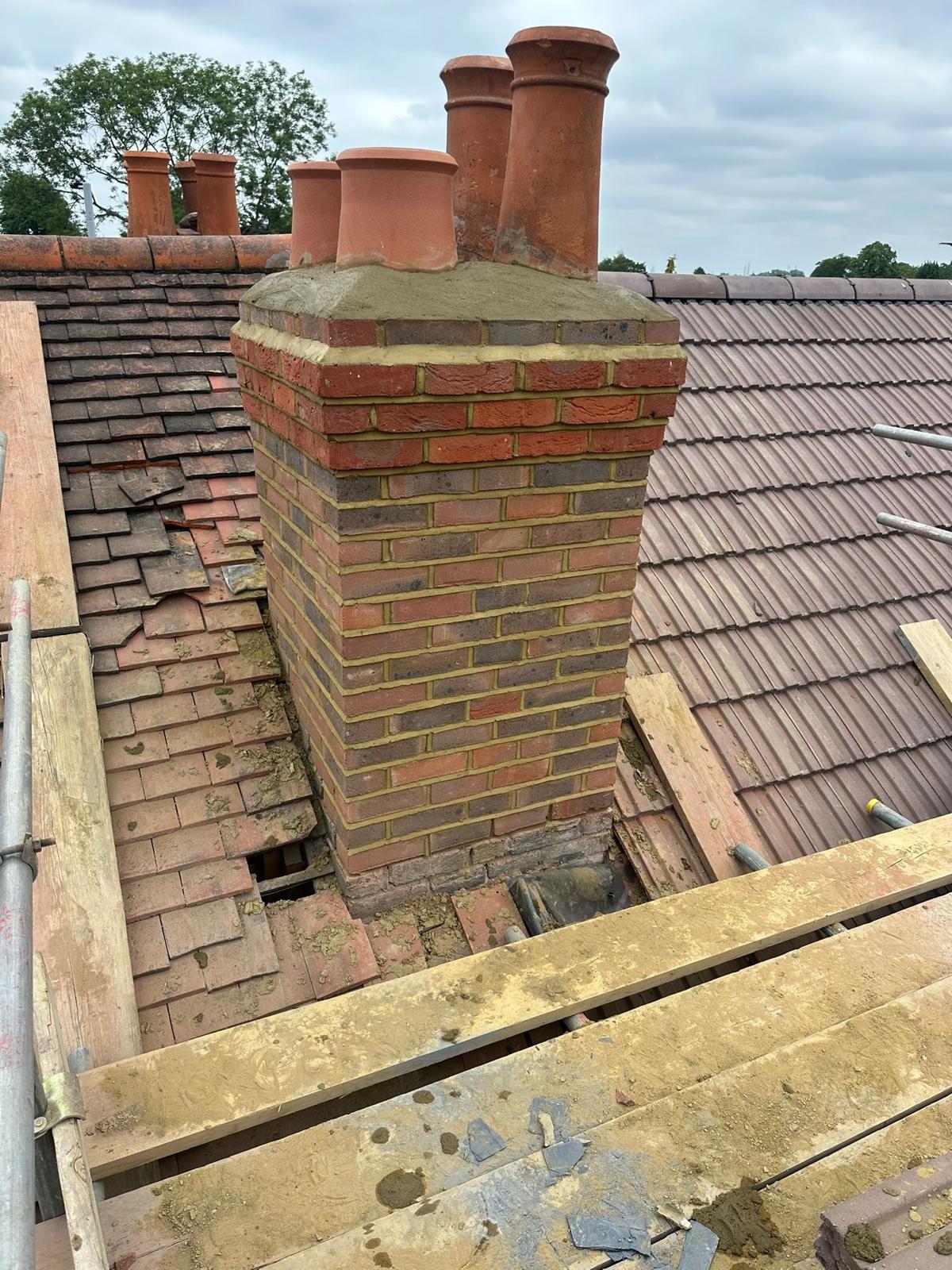 Repointed brick chimney with new pots, tiles stacked around the base ready for flashing